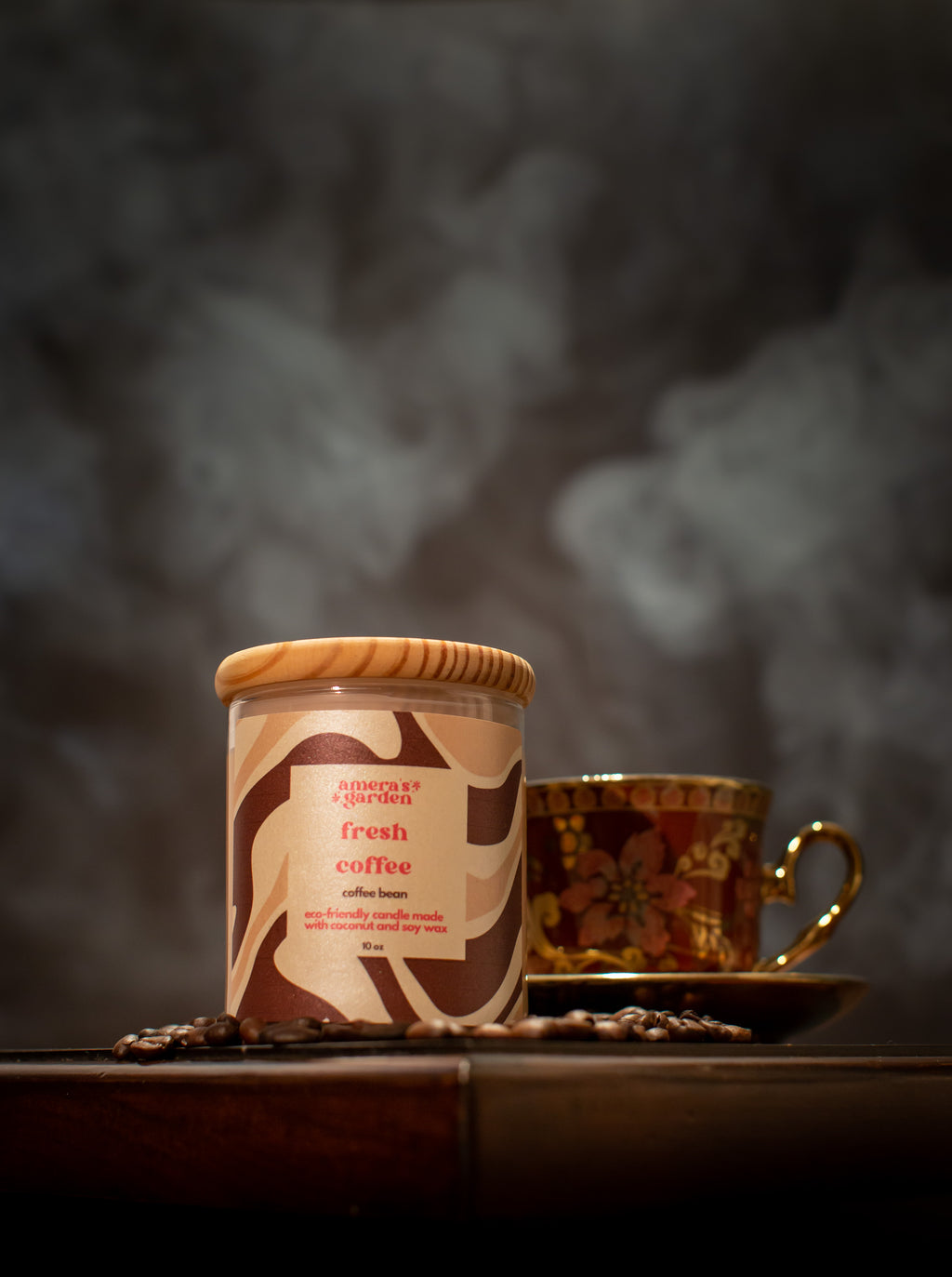 A jar of Fresh Coffee candle with a brown label, placed on a table with a cup of coffee and a teapot in the background, suggesting a theme of coffee lovers.